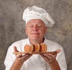 Cook chef is holding and smelling donuts baked donuts on tray
