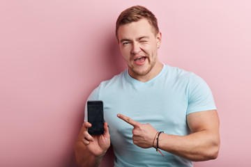 happy strong muscular smiling man in stylish blue T-shirt showing smartphone, close up portrait, isolated blue background, studio shot, gadget. lifestyle, advert, sale, discount