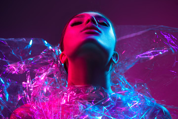 High Fashion model girl in colorful bright neon lights posing in studio through transparent film....