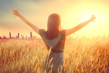 Happy autumn woman raising hands over sunset sky, enjoying life and nature. Beauty female on field looking on sun. Silhouette of girl in sunlight rays. Fresh air, environment concept. Dream of flying