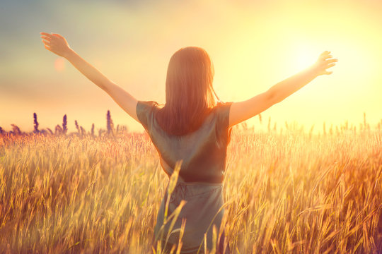 Happy autumn woman raising hands over sunset sky, enjoying life and nature. Beauty female on field looking on sun. Silhouette of girl in sunlight rays. Fresh air, environment concept. Dream of flying