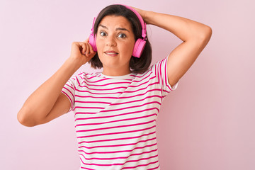 Fototapeta na wymiar Young beautiful woman listening to music using headphones over isolated pink background stressed with hand on head, shocked with shame and surprise face, angry and frustrated. Fear and upset