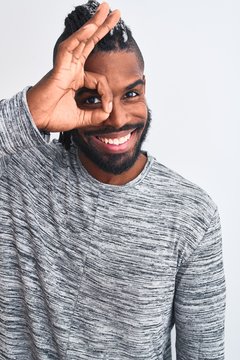 African american man with braids wearing grey sweater over isolated white background with happy face smiling doing ok sign with hand on eye looking through fingers