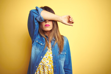Young beautiful woman standing over yellow isolated background covering eyes with arm, looking serious and sad. Sightless, hiding and rejection concept - obrazy, fototapety, plakaty