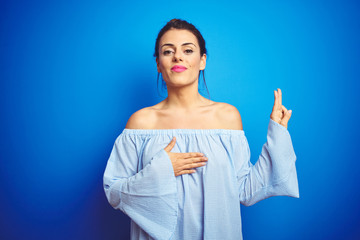 Fototapeta premium Young beautiful woman wearing bun hairstyle over blue isolated background smiling swearing with hand on chest and fingers up, making a loyalty promise oath