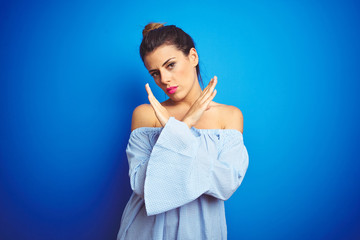 Young beautiful woman wearing bun hairstyle over blue isolated background Rejection expression crossing arms doing negative sign, angry face