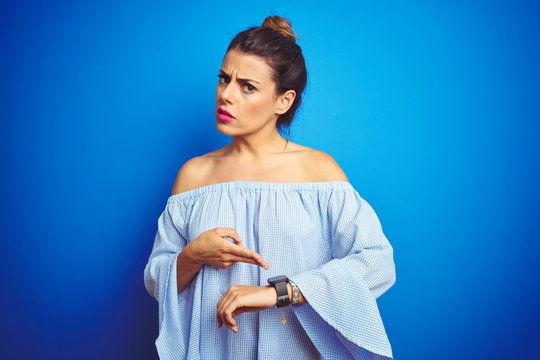 Young beautiful woman wearing bun hairstyle over blue isolated background In hurry pointing to watch time, impatience, upset and angry for deadline delay