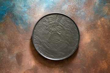 Empty rustic black stone plate on a dark concrete background. Top view with copy space.