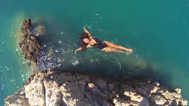 Aerial view of beautiful girl in bikini, floating in a crystal clear, blue sea water