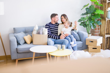 Beautiful family with kid sitting on the sofa drinking coffee at new home around cardboard boxes
