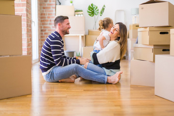 Fototapeta na wymiar Beautiful family sitting on the floor playing with his kid at new home around cardboard boxes