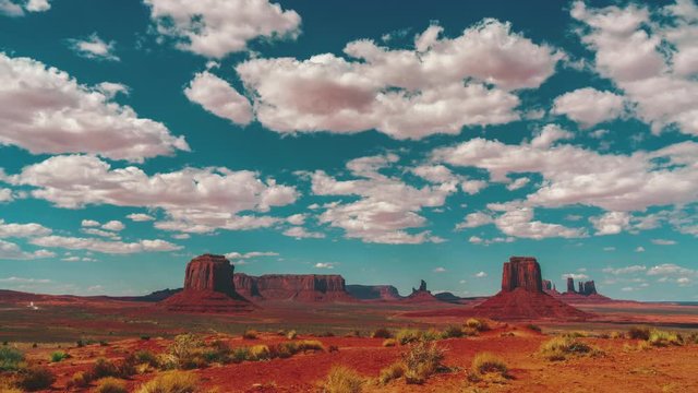 4K UHD time lapse of famous Monument Valley landmarks in Utah, USA. The clouds above the red rocks and soil in the Native American Navajo Reserve are moving fast across the blue summer sky.
