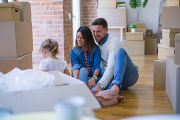 Beautiful family sitting on the floor playing with his kid at new home around cardboard boxes