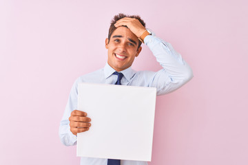 Young handsome businessman holding banner standing over isolated pink background stressed with hand on head, shocked with shame and surprise face, angry and frustrated. Fear and upset for mistake.