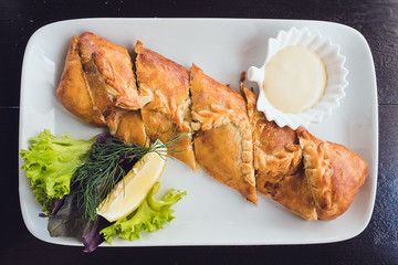 sliced puff pastry roll on a rectangular plate, garnished with greens and lemon and white sauce
