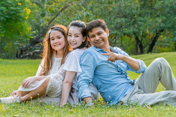 Happy Asian family portrait sitting and relaxing together in the park.