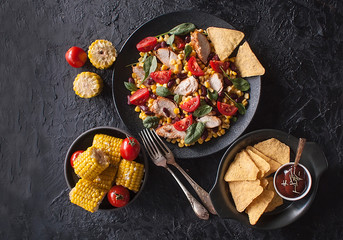 Mexican vegetable and chicken salad with nachos on black dark background. Corn, tomatoes, peppers, beans. Taco mix. The view from the top. Copy space