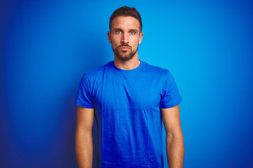 Young handsome man wearing casual t-shirt over blue isolated background Relaxed with serious expression on face. Simple and natural looking at the camera.