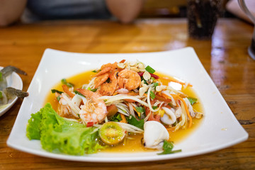 Hot and spicy seafood papaya salad in white ceramic plate on wooden table