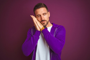 Young fitness man wearing casual sports sweatshirt over purple isolated background sleeping tired dreaming and posing with hands together while smiling with closed eyes.