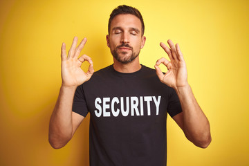 Young safeguard man wearing security uniform over yellow isolated background relax and smiling with eyes closed doing meditation gesture with fingers. Yoga concept.