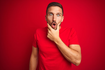 Young handsome man wearing casual t-shirt over red isolated background Looking fascinated with disbelief, surprise and amazed expression with hands on chin