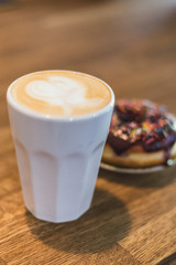 coffee with a heart made of milk and a donut on a wooden table. Coffee with a drawn heart and milk on a wooden table in a coffee shop. chocolate donut with scattering on the table next to the coffee