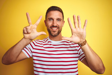 Young handsome man wearing casual red striped t-shirt over yellow isolated background showing and pointing up with fingers number eight while smiling confident and happy.