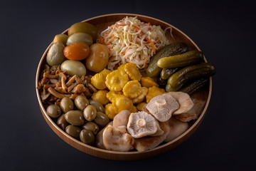 Fermented products cabbage, peppers, pickles, tomatoes, mushrooms, zucchini, garlic in a large wooden dish on a dark table. Low key. Copy space