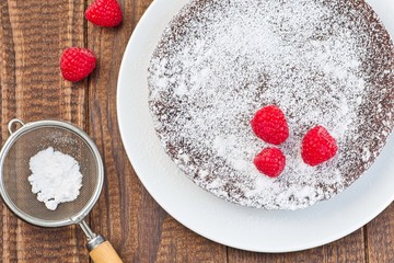 Chocolate sticky brownie cake, swedish dessert Kladdkaka, on the plate, garnished with icing sugar and raspberry, horizontal, top view