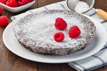 Chocolate sticky brownie cake, swedish dessert Kladdkaka, on the plate, garnished with icing sugar and raspberry, horizontal