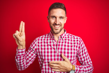 Fototapeta premium Young handsome man over red isolated background smiling swearing with hand on chest and fingers up, making a loyalty promise oath