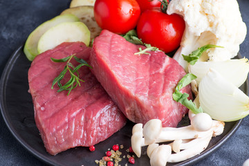 Raw beef steak on the bone with fresh vegetables in a grill pan on a concrete background, top view