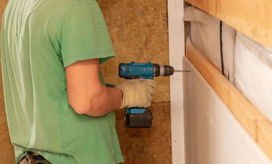 A worker fastens a sheet of drywall to the wall