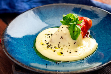Grilled eggplant with tomatoes with cheese stracciatella on blue plate. Italian recipe