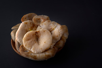 Salted mushrooms in a wooden plate on a dark table. Copy space. Low key