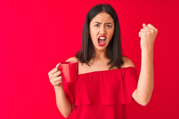 Young beautiful chinese woman drinking cup of coffee standing over isolated red background annoyed and frustrated shouting with anger, crazy and yelling with raised hand, anger concept