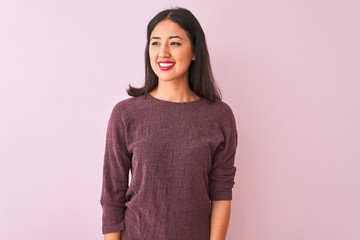 Young chinese woman wearing purple sweater standing over isolated pink background looking away to side with smile on face, natural expression. Laughing confident.