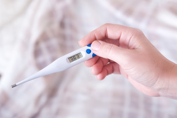 Closeup shot of a woman looking at thermometer. Female hands holding a digital thermometer. Girl measures the temperature. Shallow depth of field with focus on thermometer.