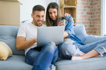 Young couple moving to a new home relaxing sitting on the sofa using computer laptop, smiling happy for moving to new apartment