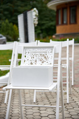 Outdoor wedding decorations, white chairs and a large white wooden box with original carvings.