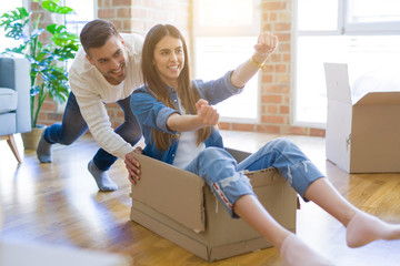 Young couple moving to a new home, having fun riding cardboard boxes