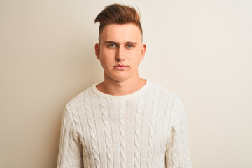 Young handsome man wearing winter sweater standing over isolated white background with serious expression on face. Simple and natural looking at the camera.