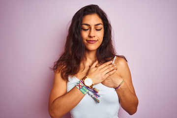 Naklejka premium Young beautiful woman wearing white t-shirt standing over isolated pink background smiling with hands on chest with closed eyes and grateful gesture on face. Health concept.