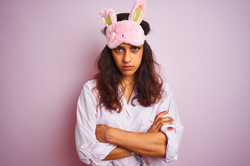 Young beautiful woman wearing pajama and sleep mask over isolated pink background skeptic and nervous, disapproving expression on face with crossed arms. Negative person.