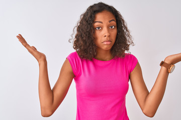 Young brazilian woman wearing pink t-shirt standing over isolated white background clueless and...