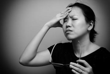 Asian woman holding glasses, suffer from having a strong headache and fever, poor sight, farsightedness, myopia. Black and white tone