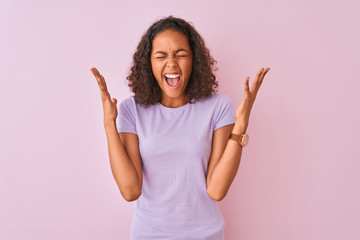 Young brazilian woman wearing t-shirt standing over isolated pink background celebrating mad and...