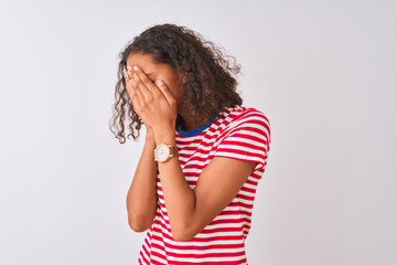 Young brazilian woman wearing red striped t-shirt standing over isolated white background with sad expression covering face with hands while crying. Depression concept.