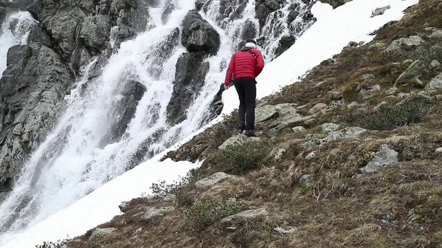 Man walk to waterfall near Susch pass near Davos in Switzerland to take photo. Filmed in slow motion.
